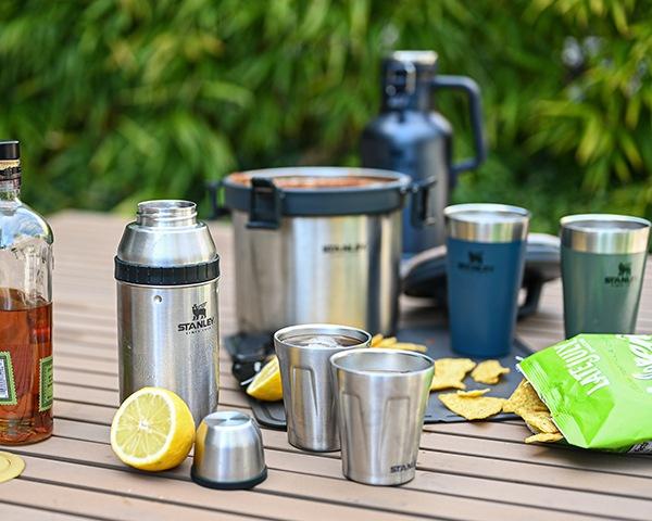 Outdoor table set up for a party with barware and the Adventure Stay Hot Camp Crock.